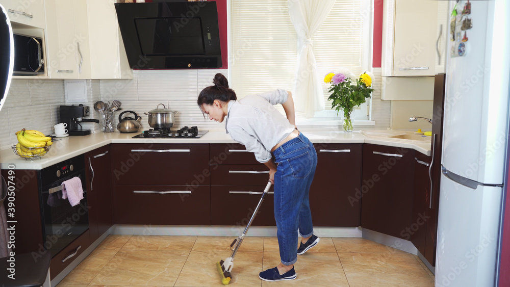 A young girl is cleaning the kitchen at home, washing the marble slab with a mop, tired from work.