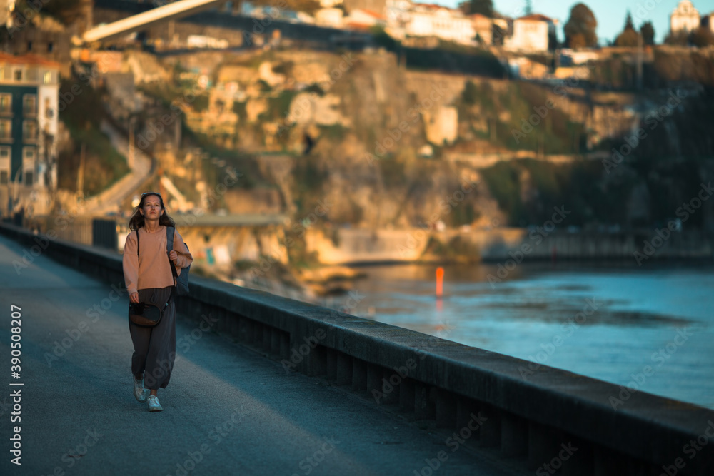 A young woman walks along the city's river embankment. Porto, Portugal.