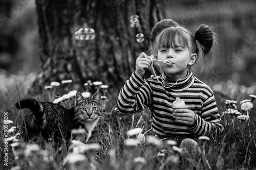 Little girl playing with a cat in the grass. Black and white photography.