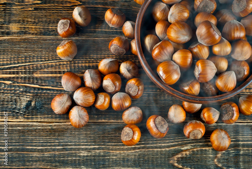 Hazelnuts in a bowl on a brown wooden background. Lots of nuts on an old shabby board. Blue smoke and steam on the table.