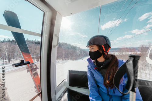 Ski resorts open for winter sports following coronavirus restriction guidelines. Woman tourist wearing face mask inside cabin lift on mountain slope going skiing.
