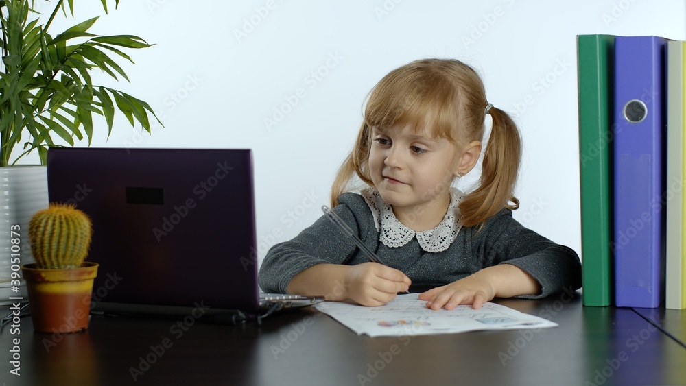 Child schoolgirl learns lessons at home sitting at table using digital laptop computer. Portrait of kid girl distance education. Studying during coronavirus quarantine. White background Child schoolgirl learns lessons at home sitting at table using digital laptop computer. Portrait of kid girl distance education. Studying during coronavirus quarantine. White background