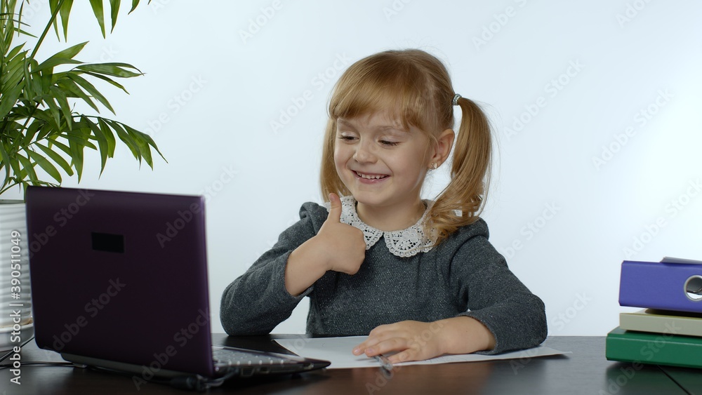 Child schoolgirl learns lessons at home sitting at table using digital laptop computer. Portrait of kid girl distance education. Studying during coronavirus quarantine. White background Child schoolgirl learns lessons at home sitting at table using digital laptop computer. Portrait of kid girl distance education. Studying during coronavirus quarantine. White background