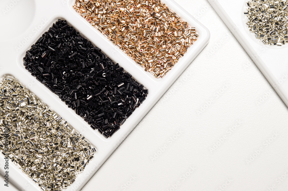 Palette with beads in three colors: silver, black, gold. Shiny glass beads on a white background in a white palette, top view. Horizontal photography. Palette with beads in three colors: silver, black, gold. Shiny glass beads on a white background in a white palette, top view. Horizontal photography.