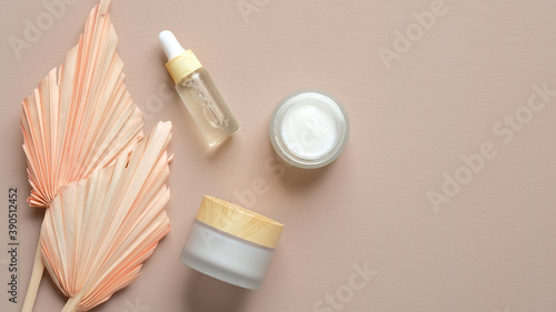 Natural organic cosmetic set. Essential oil dropper bottle, moisturizer cream jars and dry flowers on pastel beige background. Flat lay, top view.
