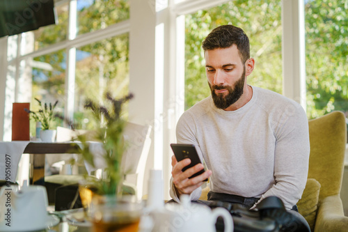 Portrait of adult good looking caucasian man sitting at cafe in day using mobile phone - Male with beard online date on internet while waiting sending love in video call - dating and meeting concept