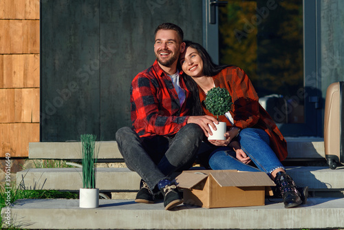 Young couple sitting on stairs having fun unpacking boxes after moving to new house.
