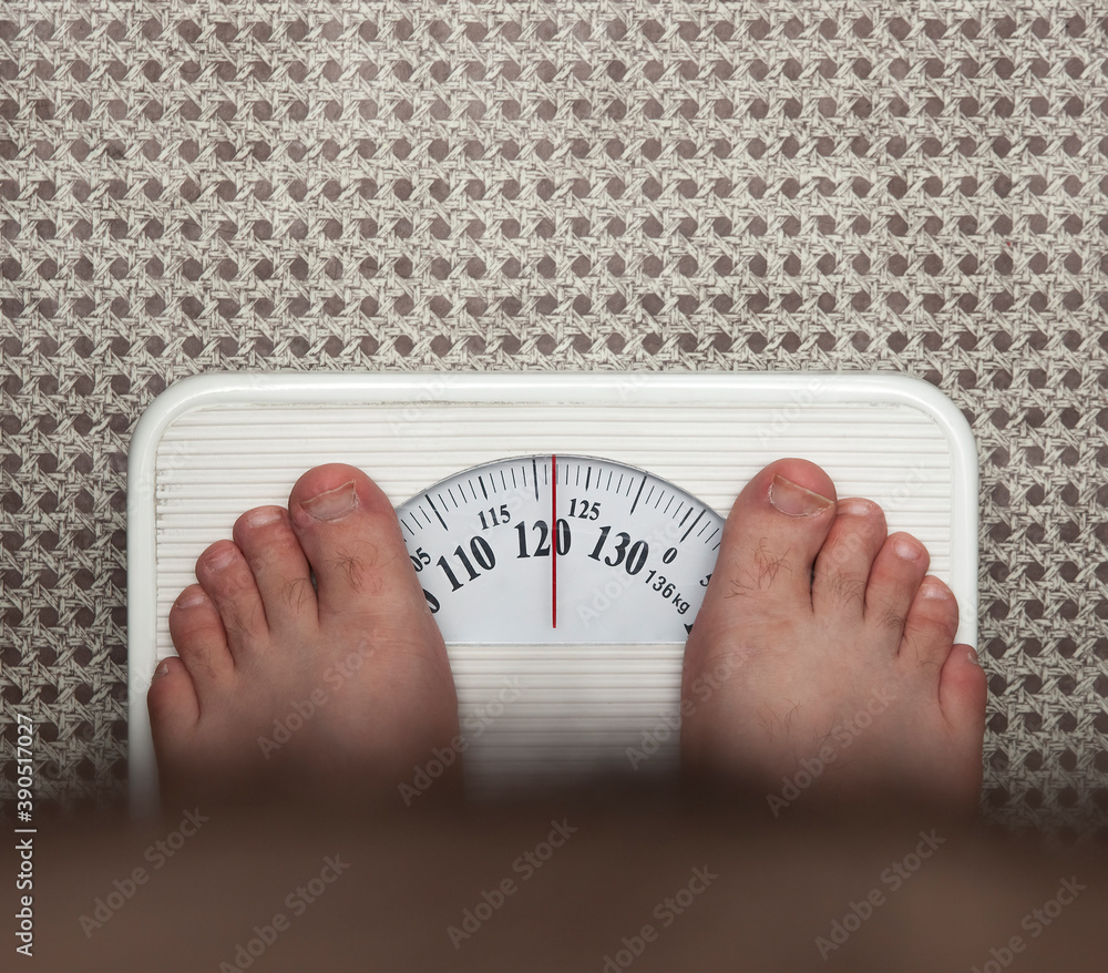 Fat man measuring his weight on a scale. top view.bare feet of an overweight  man