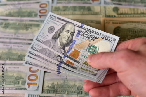 Stack Of 100 Dollars Banknotes Bundles in a man's hand against the background of American banknotes