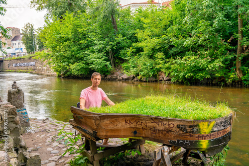 Young man playing abandoned gran piano covered with grass, rundown piano by a river bank Vilnia river in Uzupis artists quarter in Vilnius photo