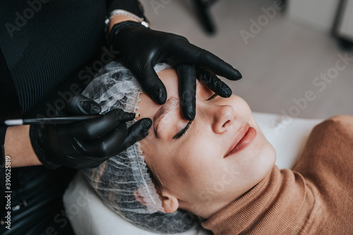 Eyebrows microblading concept. Cosmetologist preparing young woman for eyebrow permanent makeup procedure.