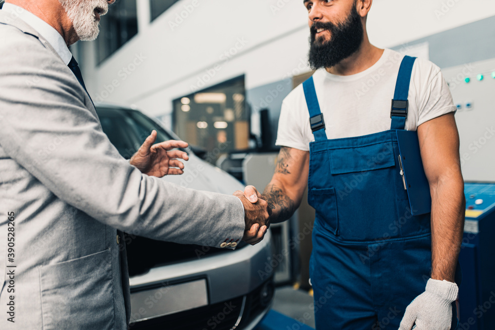 Obraz premium Car mechanic talking with senior business man costumer during periodic car condition check. Technical inspection.