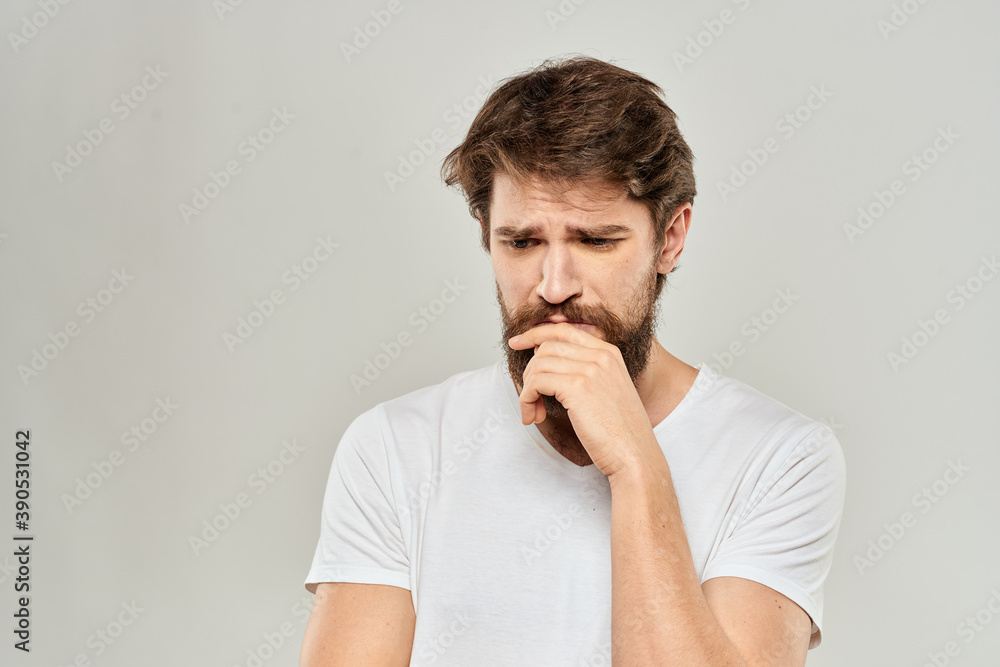 A man in a white t-shirt with a beard emotions displeased facial expression light background A man in a white t-shirt with a beard emotions displeased facial expression light background
