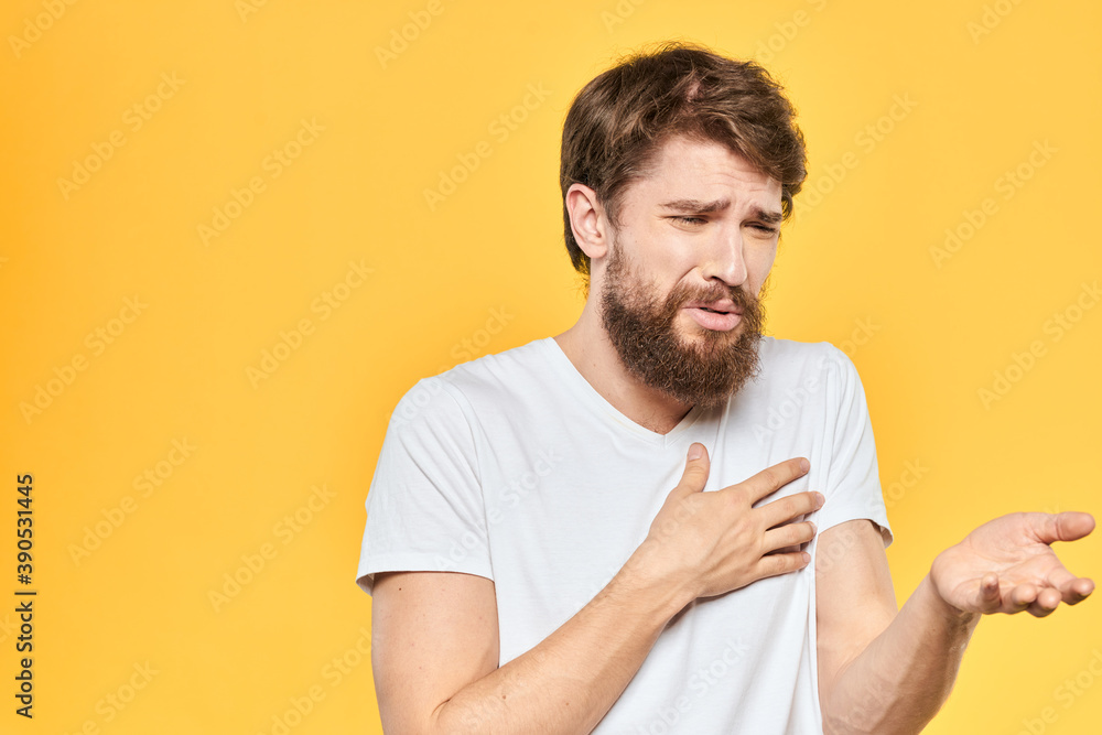 Man in white t-shirt emotions studio gestures with hands displeased facial expression yellow background Man in white t-shirt emotions studio gestures with hands displeased facial expression yellow background