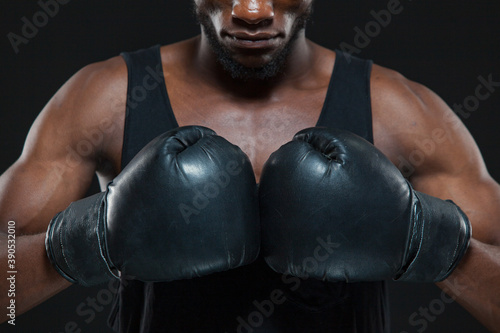 Front view shot of young African American boxer wearing gloves is posing isolated on a dark background © satyrenko