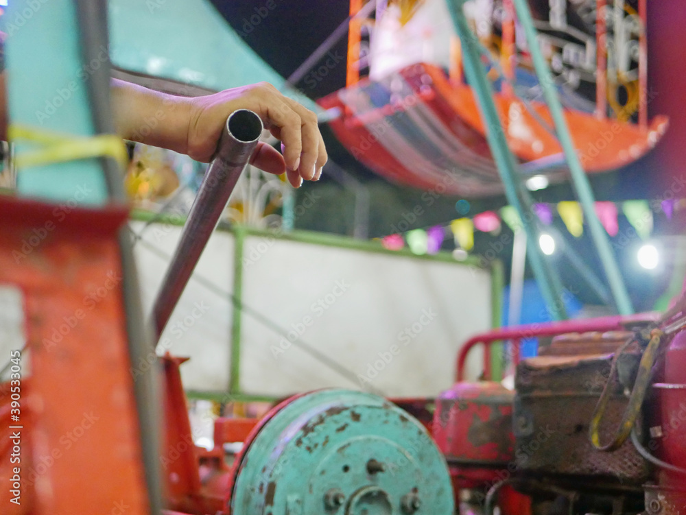 A hand of a man resting on a controller bar / stick controlling a ferris wheel in an outdoor night fair