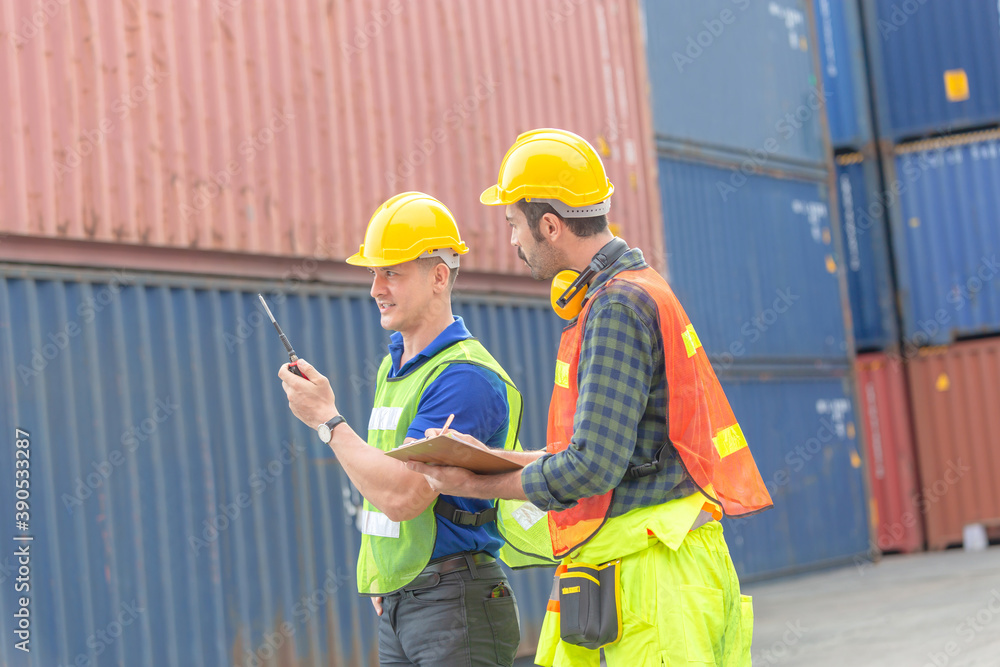 Engineer man in hardhat and safety vest talks on two-way radio, foreman worker holding clipboard checklist at containers cargo, Teamwork concept Engineer man in hardhat and safety vest talks on two-way radio, foreman worker holding clipboard checklist at containers cargo, Teamwork concept