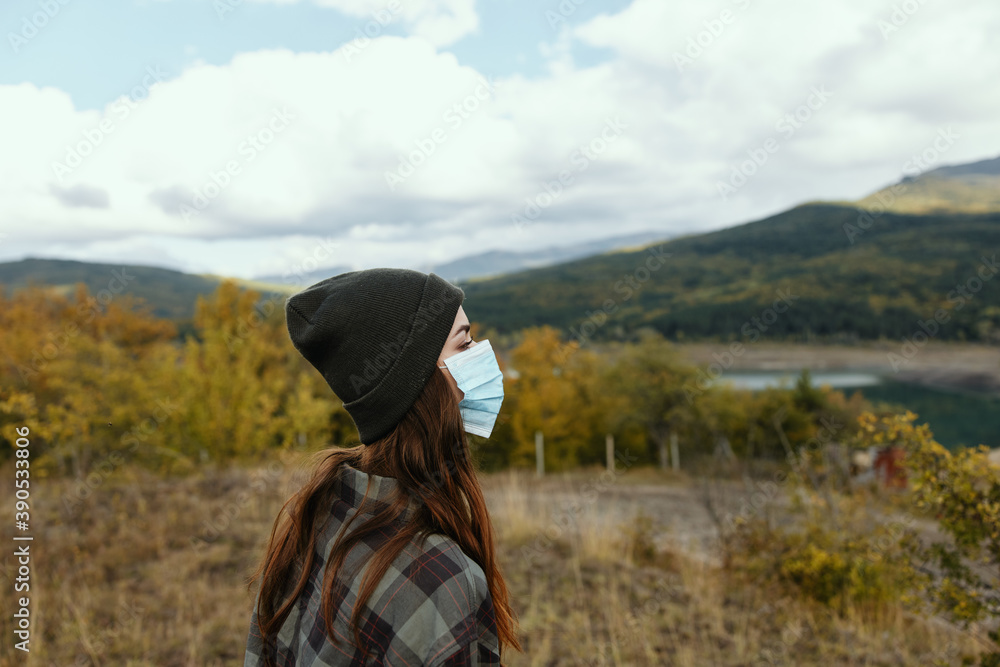 Woman in warm caps in the autumn forest with a medical mask on her face