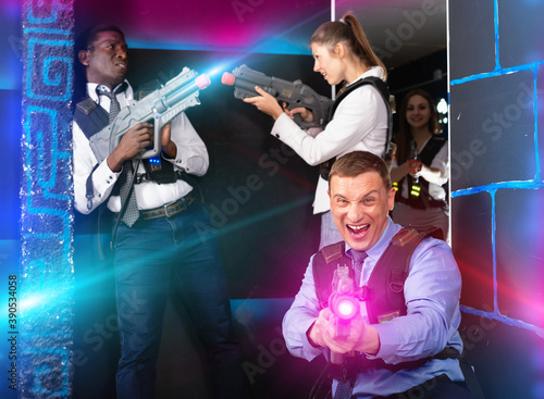 Happy smiling men and women in business suits playing laser tag emotionally in dark room © JackF