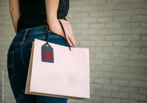 Woman holding a paper bag with tag black Friday. Back view of slender female butt in blue jeans. Concept of shopping, seasonal discounts.