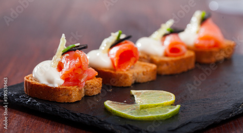 Canapes with salmon and black olives served on toasted baguette with cream sauce, greens and lemon