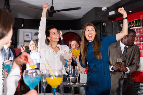 Young glad cheerful positive attractive women with cocktails having fun with workmates on office party at nightclub