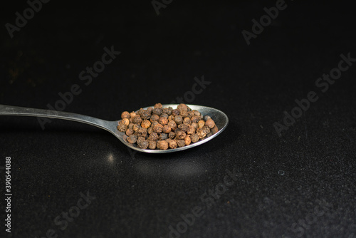 Black pepper in a spoon on black background