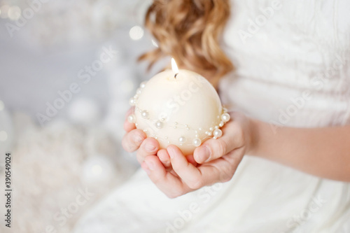 Burning candle in the hands of a girl.  Christmas decor. Child's hands holding beautiful candle with fire. Christmas time. New Year and Winter holidays. Copy space