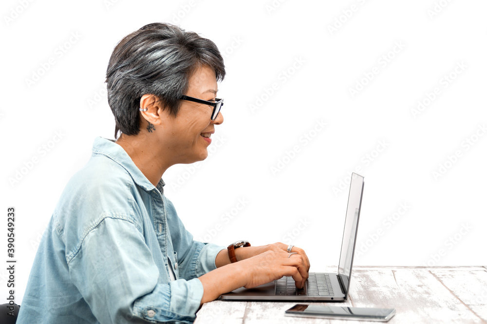 Happy Senior businesswoman wearing glasses working on a laptop in office. Asian mature female smiling at a laptop computer while sitting at her desk. Isolated white background. Active Elderly concept Happy Senior businesswoman wearing glasses working on a laptop in office. Asian mature female smiling at a laptop computer while sitting at her desk. Isolated white background. Active Elderly concept