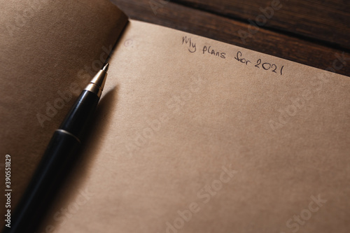 Notepad with the inscription on the page "My plans for 2021" with a pen on a dark wooden background