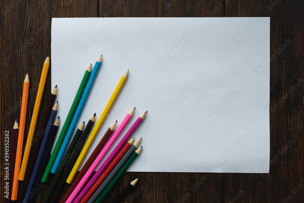 Obraz premium Blank, white sheet of paper with colored pencils on dark wooden background