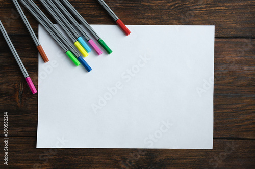 Blank, white sheet of paper with colored markers on dark wooden background