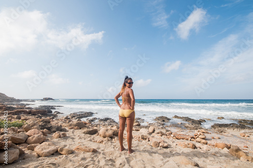 Pretty woman in bikini standing by the sea, preparing to enter the water.