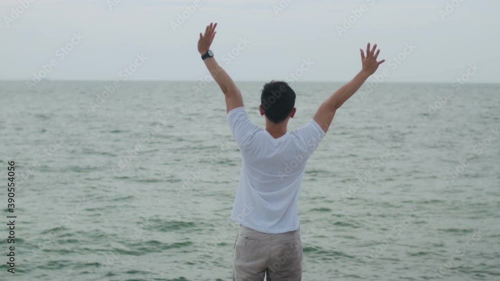 Happy asian male celebration success with raise arms into the air on the holiday weekend. Handsome man caucasian traveler standing on the beach and looking seascape. Happy asian male celebration success with raise arms into the air on the holiday weekend. Handsome man caucasian traveler standing on the beach and looking seascape.