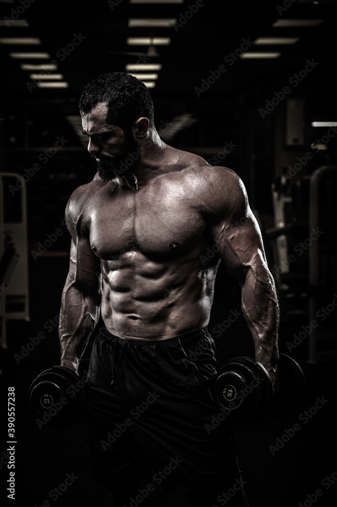 Fototapeta premium strong young athlete with beard in sport gym holding dumbbells during heavy weight training workout