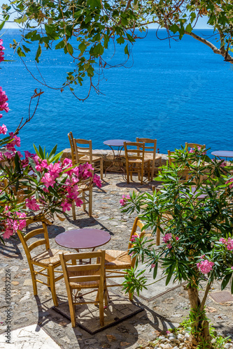 Fototapeta Naklejka Na Ścianę i Meble -  Traditional cafe exterior in the fortified medieval  castle of Monemvasia. Iron tables and wooden chairs with the view of the  aegean sea in the background.