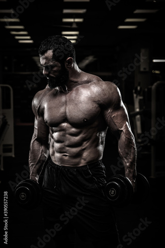 strong young athlete with beard in sport gym holding dumbbells during heavy weight training workout