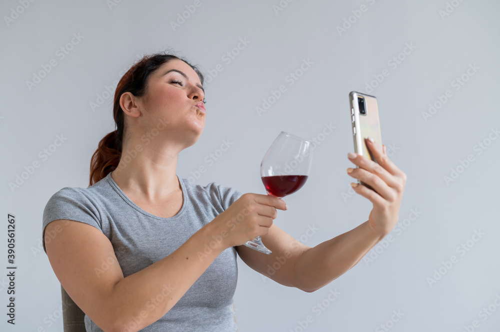 Caucasian woman drinks red wine and communicates with friends via video communication on a smartphone. The quarantined girl celebrates the holiday via an online conference Caucasian woman drinks red wine and communicates with friends via video communication on a smartphone. The quarantined girl celebrates the holiday via an online conference
