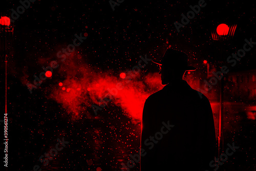 dark silhouette of a man in a hat in the rain on a night street in a city photo