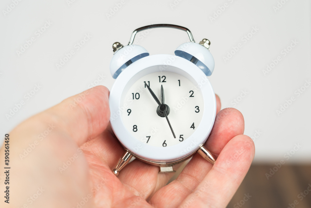 Small white alarm clock with the time five to twelve, hand-held Small white alarm clock with the time five to twelve, hand-held