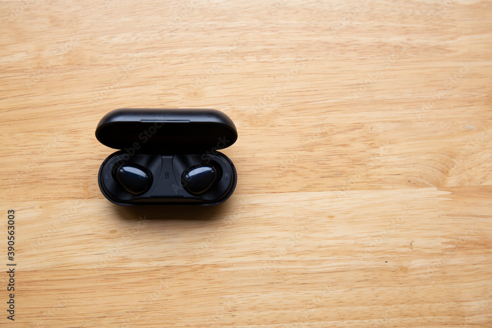 Wireless Earbuds with Charging Case on wooden background top view 