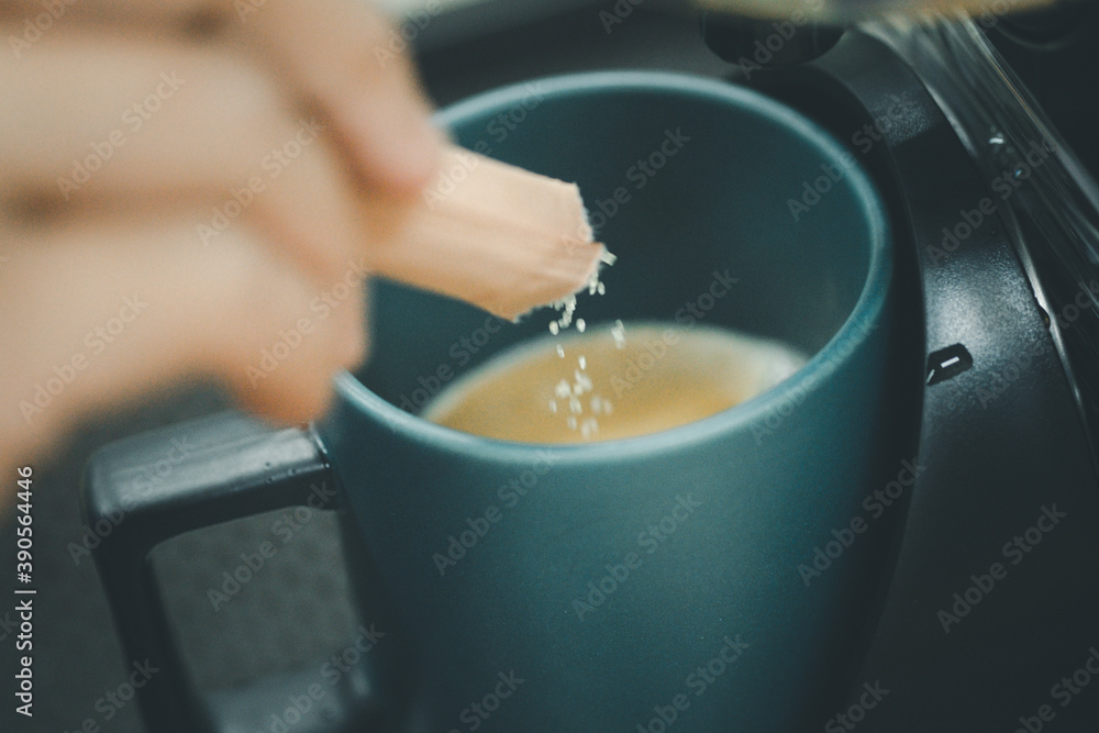 Hand pouring a sugar packet into a cup of coffee.