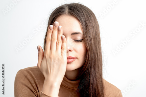Portrait of beautiful young woman with closed eyes covering one eye by her hand on white background