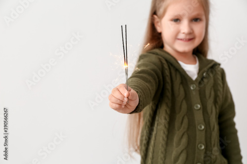 Cute little girl with Christmas sparklers on light background