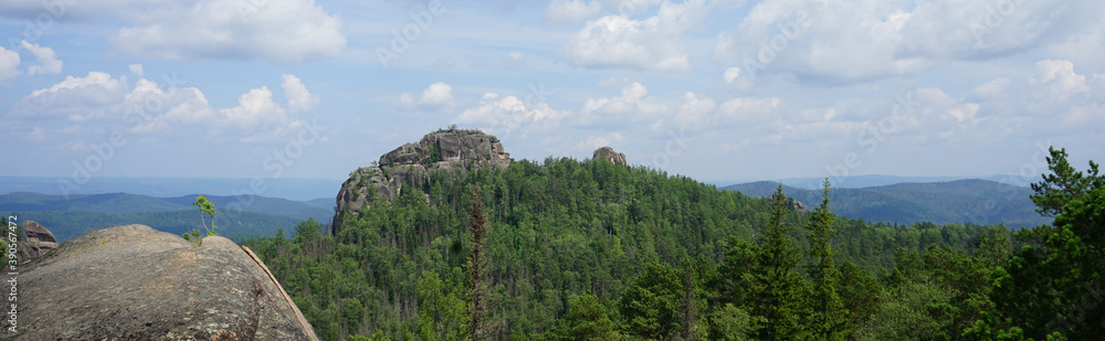 View from the top of the cliff to the Siberian taiga. Rocks and blue sky with clouds. Mountain landscape. Stolby National Park in Krasnoyarsk. Rock.