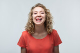 Portrait of cute blonde girl sticking out her tongue at camera. Human emotions concept. Studio shot, white background