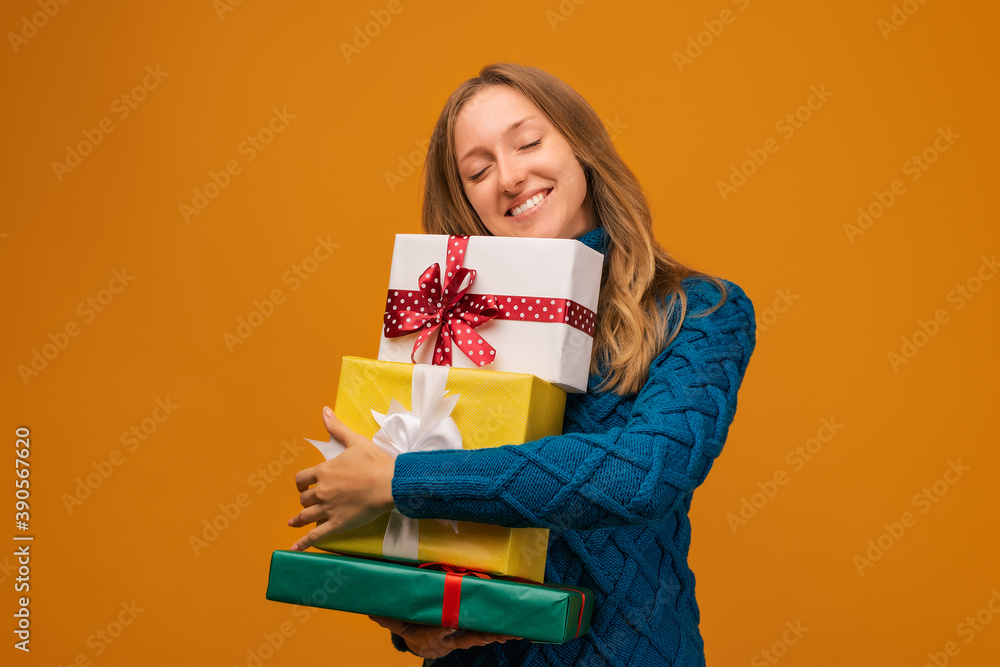Portrait of a charming young woman in knitted sweater holding stack of present boxes. Studio shot, yellow background Portrait of a charming young woman in knitted sweater holding stack of present boxes. Studio shot, yellow background