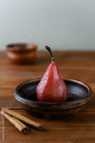 Poached pear in red wine on a brown clay bowl.