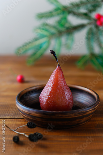 Pear in red wine in a brown bowl on the background of a Christmas tree branch.