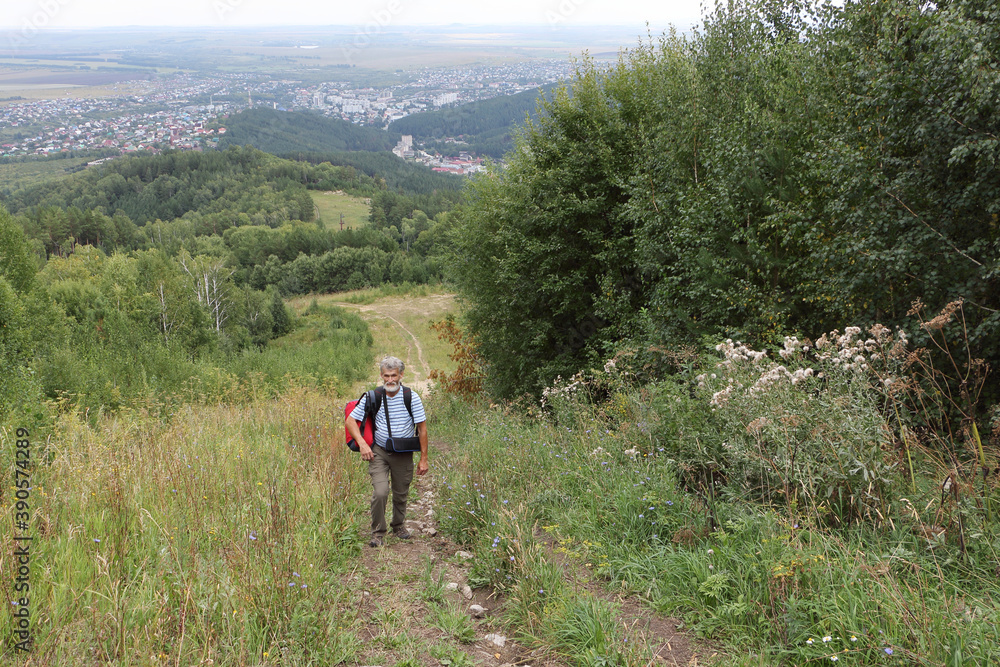 Man with a backpack climbing the trail up the mountain Tserkovka, Belokurikha city, Russia